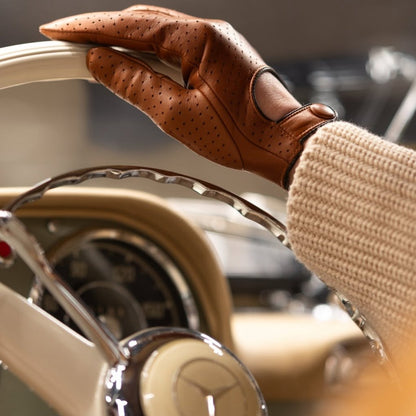 Hand wearing a brown leather glove holding a car steering wheel with a blurred background